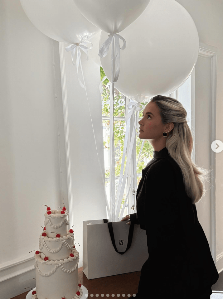 Woman looking at white balloons and a three-tiered cake.