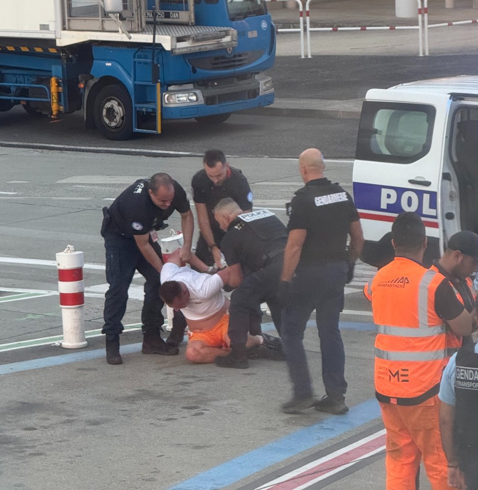 Police officers arresting a man on an airport tarmac.