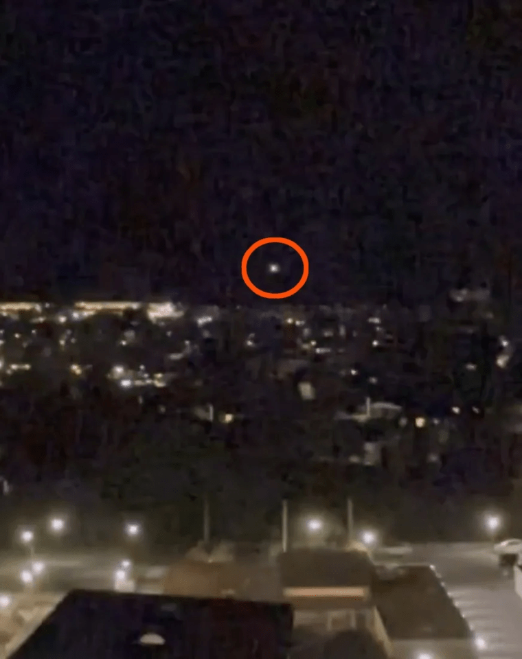 Night photo of a cityscape with a bright light circled in orange in the sky.