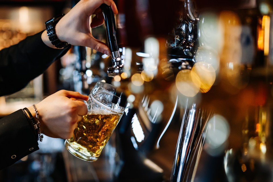 Hand of a bartender pouring beer from a tap into a glass.
