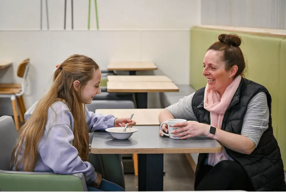 Woman and girl sitting at a table in a cafe, enjoying a meal and a drink.