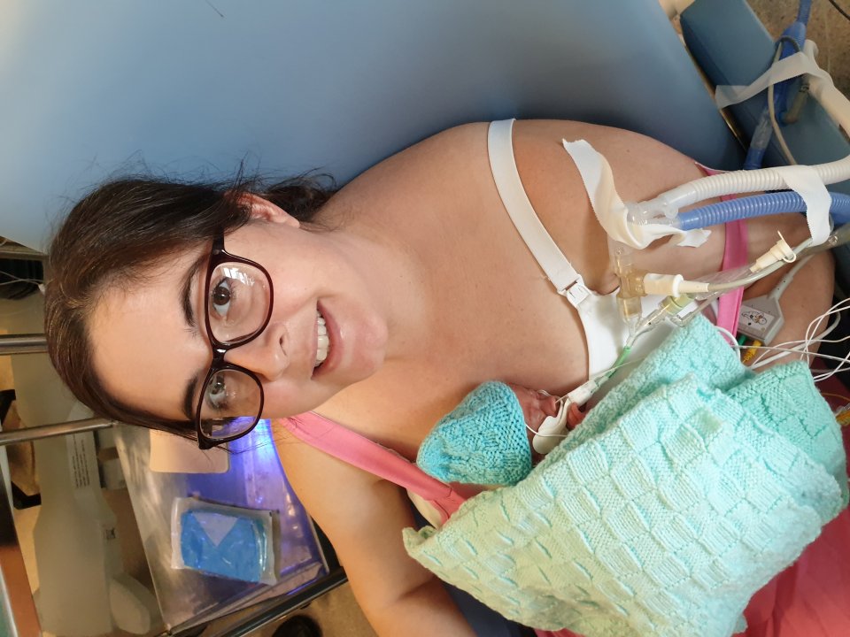 Natasha Hewitt holding her 8-day-old baby, Harry, while connected to medical tubes.
