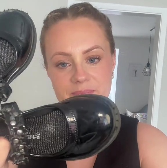A woman holding up a pair of scuffed black school shoes.