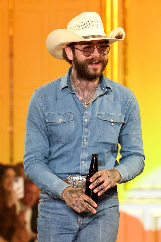 Post Malone walking a runway, holding a beer bottle.