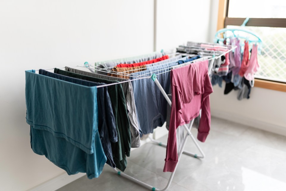 Laundry drying on an indoor rack next to a window.