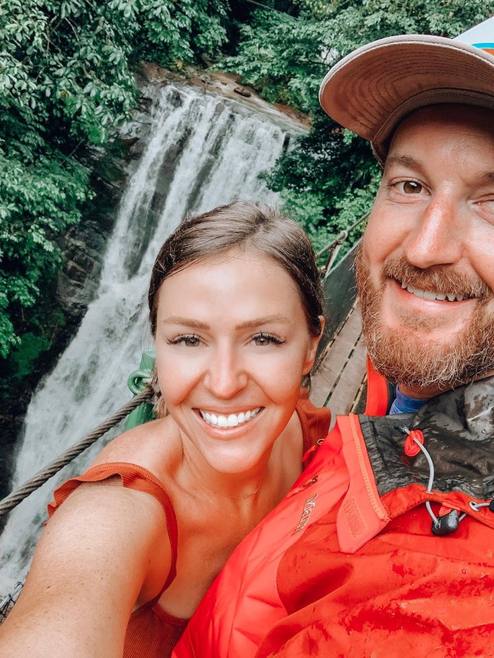 Woman and man smiling for a selfie with a waterfall in the background.