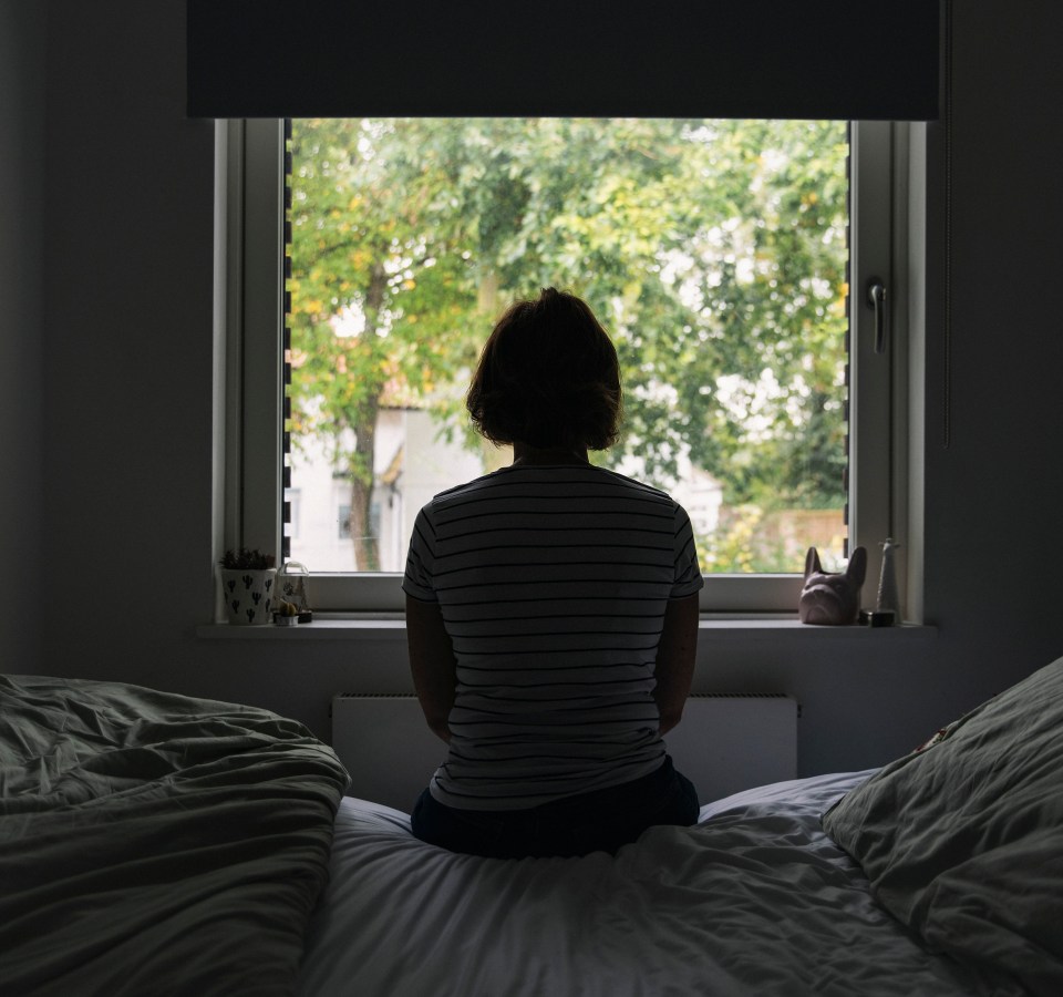 Woman sitting on bed, looking out window.