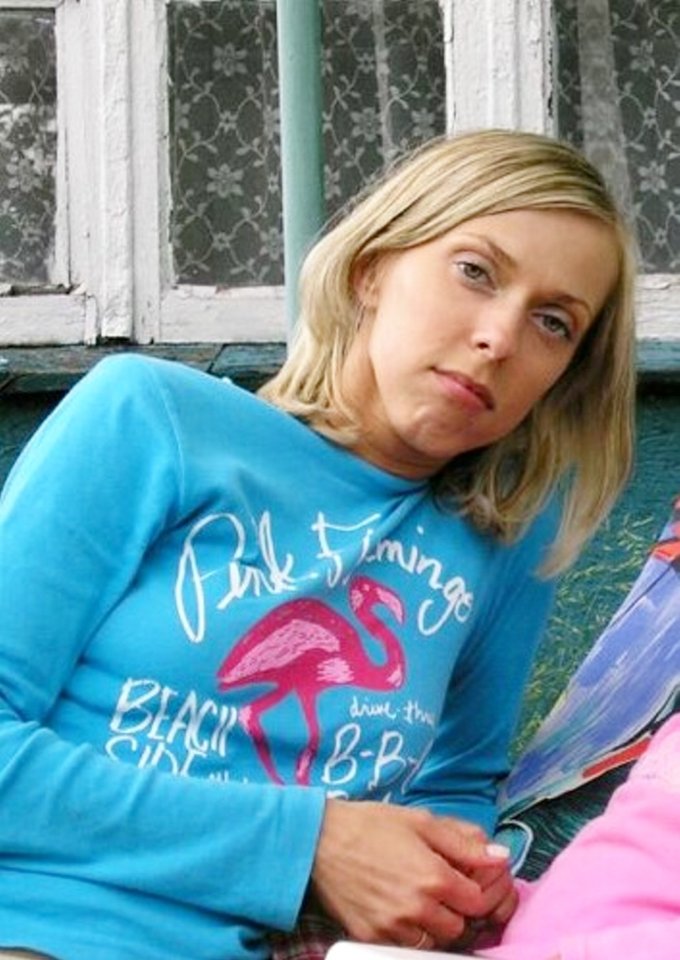 Malgorzata Wnuczek, a blonde woman wearing a blue long-sleeved shirt with a pink flamingo design, leans against a patterned window.