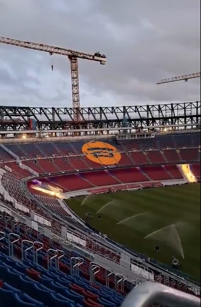 Stadium under construction with a large orange logo on the seating.