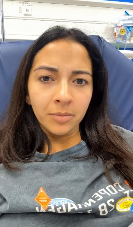 A woman in a hospital gown looks at the camera while sitting in a blue chair.