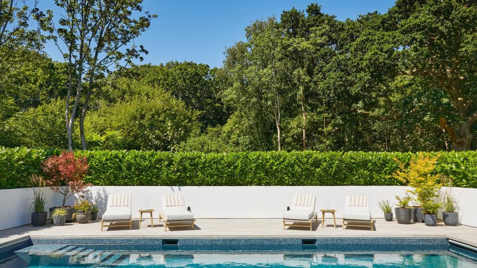 Poolside lounge chairs overlooking a hedge and woods.