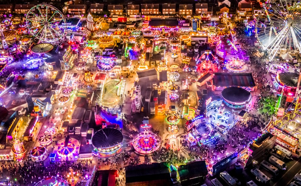 Aerial view of a brightly lit Hull Fair at night, with multiple rides and attractions, including Ferris wheels.