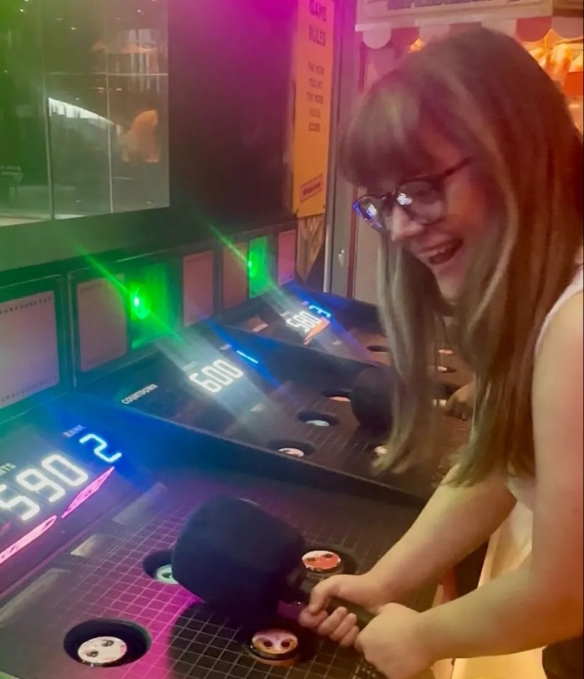 A person laughing while playing a whack-a-mole arcade game.