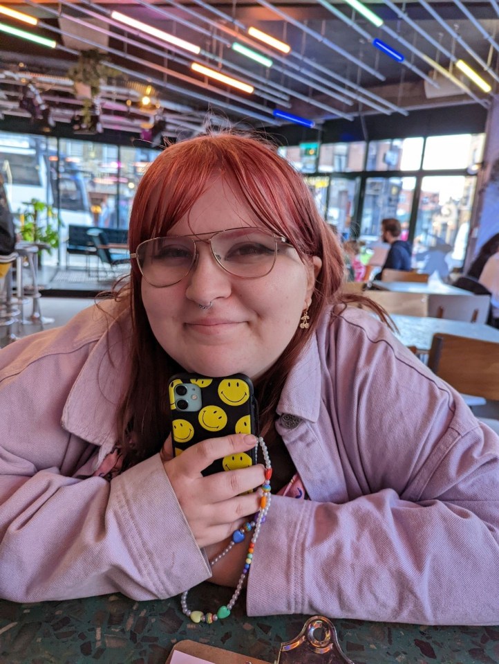 Zoe Nunn, a politics student, smiles at the camera while holding her phone with a smiley face case.
