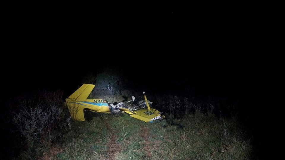 Wreckage of a small yellow and blue plane on the ground at night.