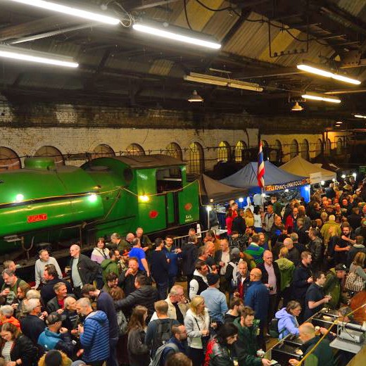 A large crowd of people gathered in a train shed with a green locomotive.