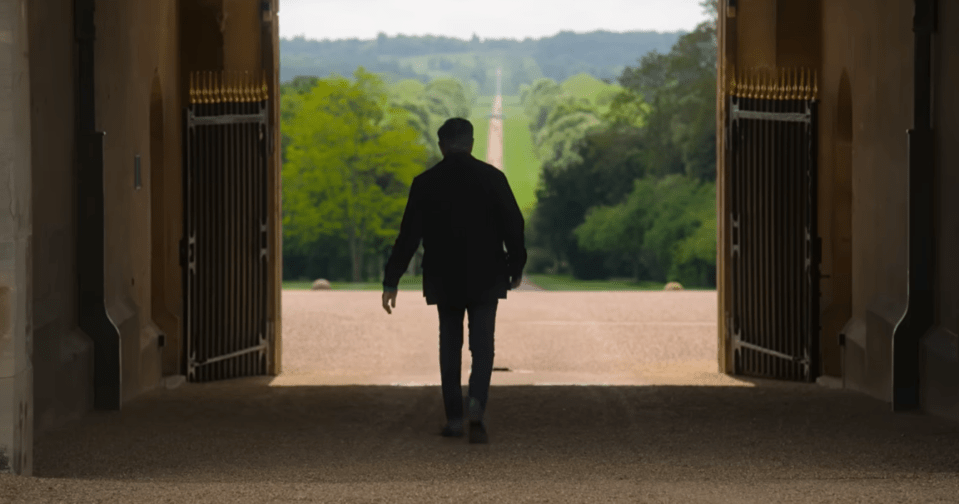 Person walking through open gates toward a long driveway.