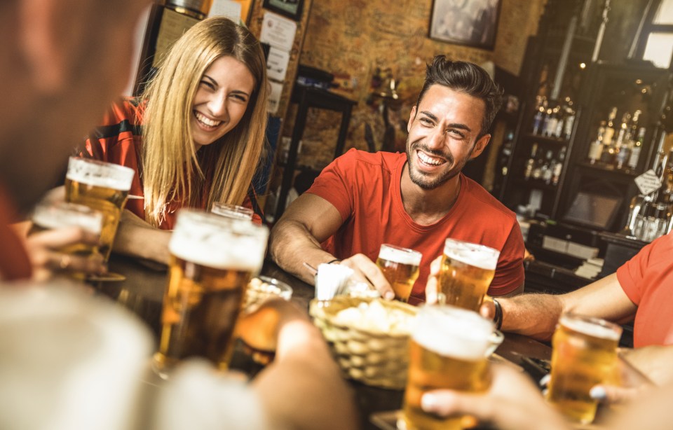 Four friends smiling and holding beers in a bar.