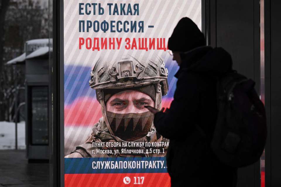 Person at a bus stop looking at an advertising screen promoting contract military service in the Russian army.