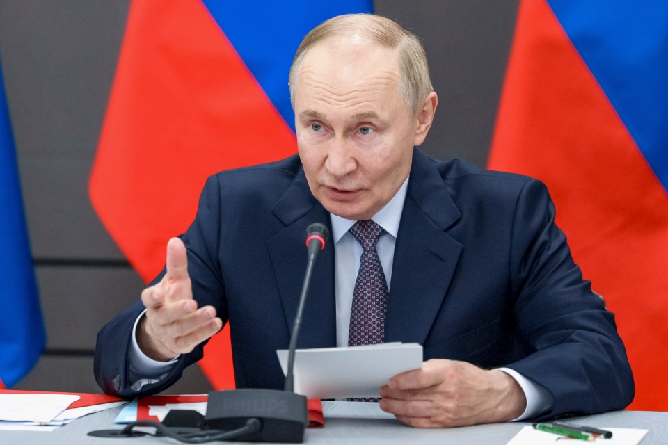 Russian President Vladimir Putin speaks at a meeting, gesturing with one hand and holding papers in the other.