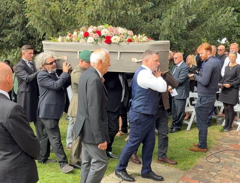 Pallbearers carrying a casket covered in flowers at a funeral.