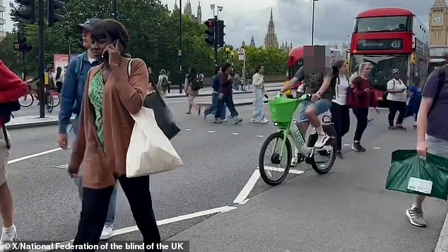 A cyclist weaves through pedestrians trying to cross Westminster Bridge Road in London