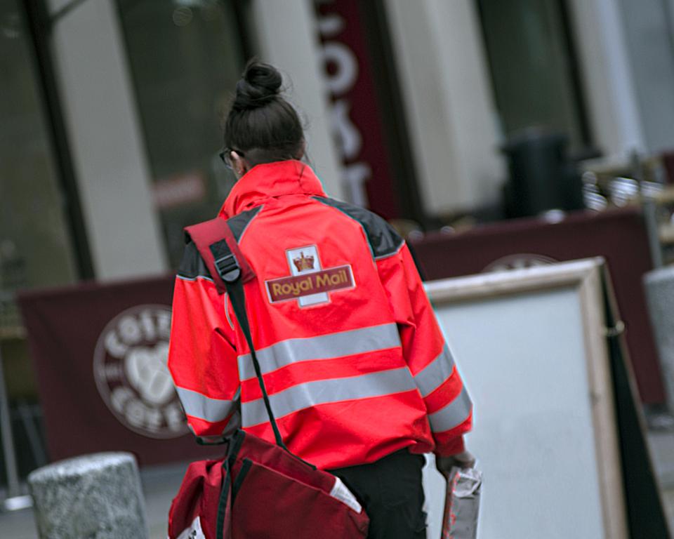 KF8D5N Royal Mail postman postwoman delivering letters street doorway costa coffee