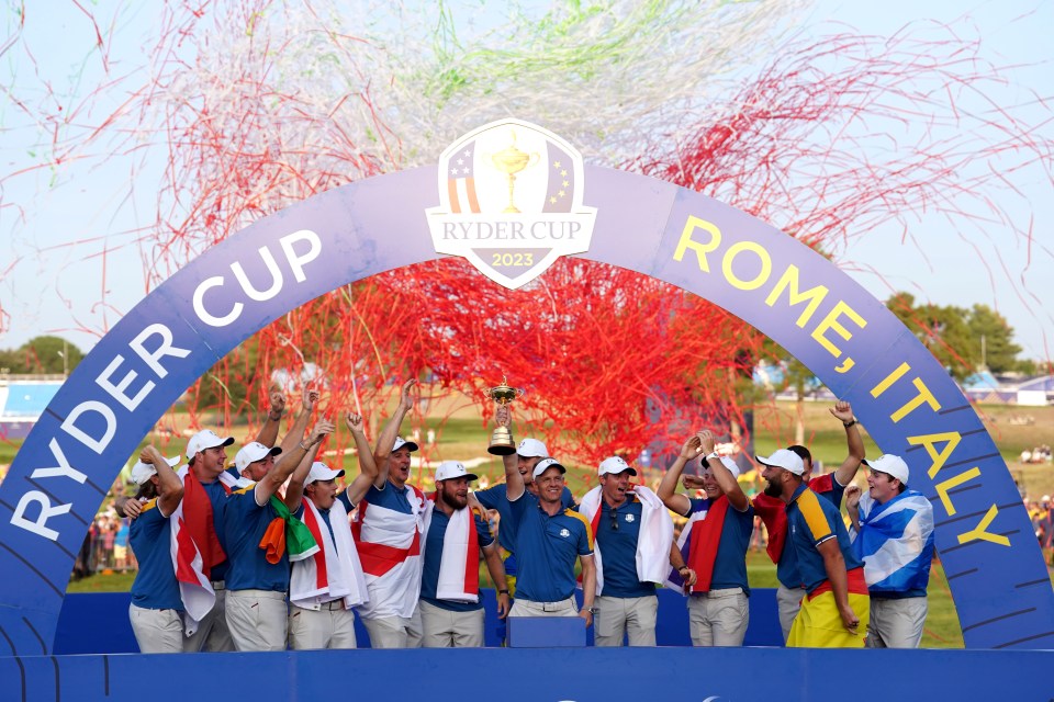 Team Europe golf players lifting the Ryder Cup trophy under an arch that reads "Ryder Cup 2023 Rome, Italy" as confetti falls.