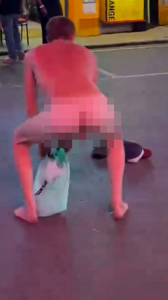 A naked man thrusting his hips in the middle of a street.