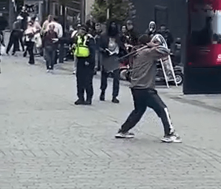 Man swinging a spade in the street while people watch.