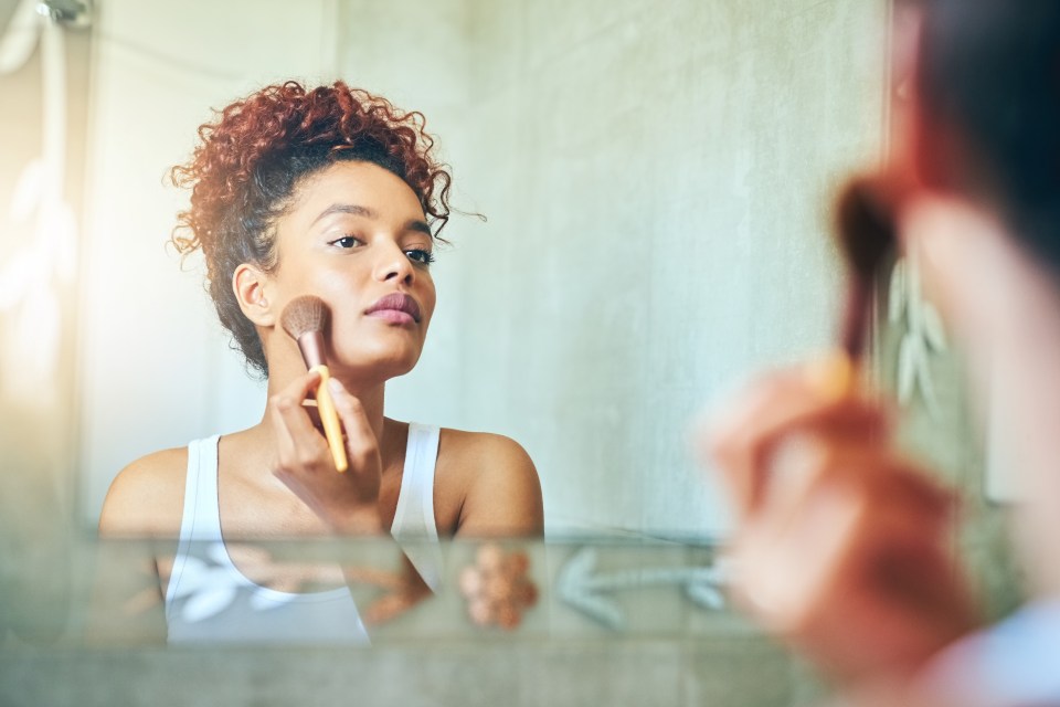 Young woman applying makeup in bathroom mirror.