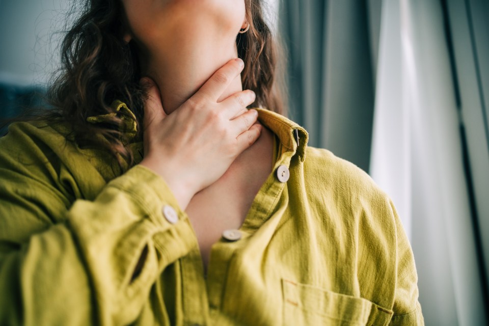 Woman holding her throat, experiencing a sore throat.