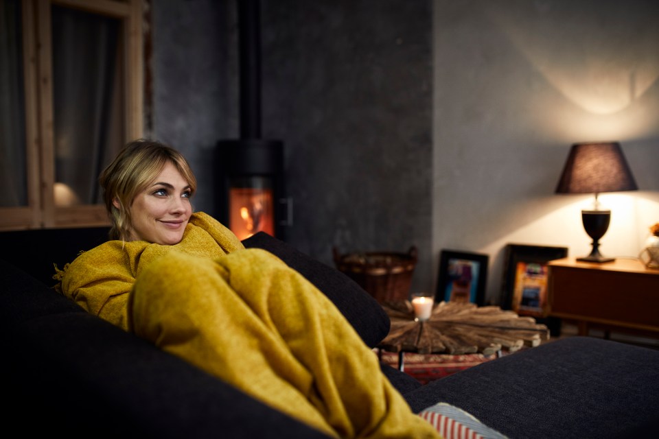 Woman relaxing on a couch under a yellow blanket.