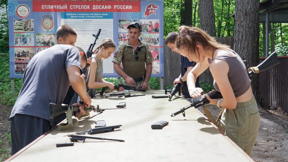 Children and teenagers learn to assemble and disassemble rifles with an instructor.