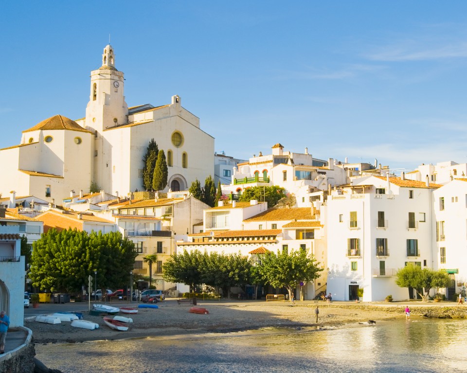 Cadaqués town with a church and boats on the beach.