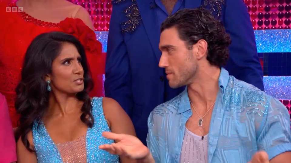 A woman in a blue sparkly dress looking displeased at a man in a blue sparkly shirt, who is looking at her with a questioning expression.
