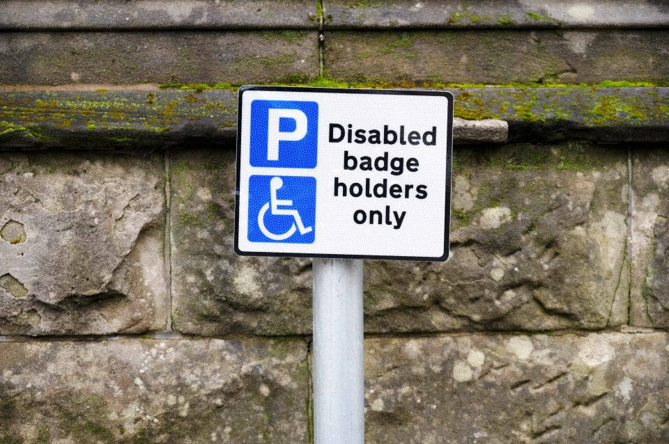 A sign for disabled blue badge holders only parking against a mossy stone wall.