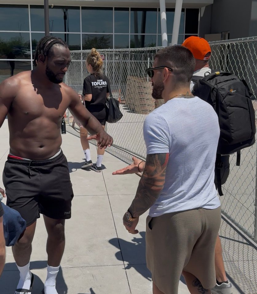 Two shirtless men talking outdoors.