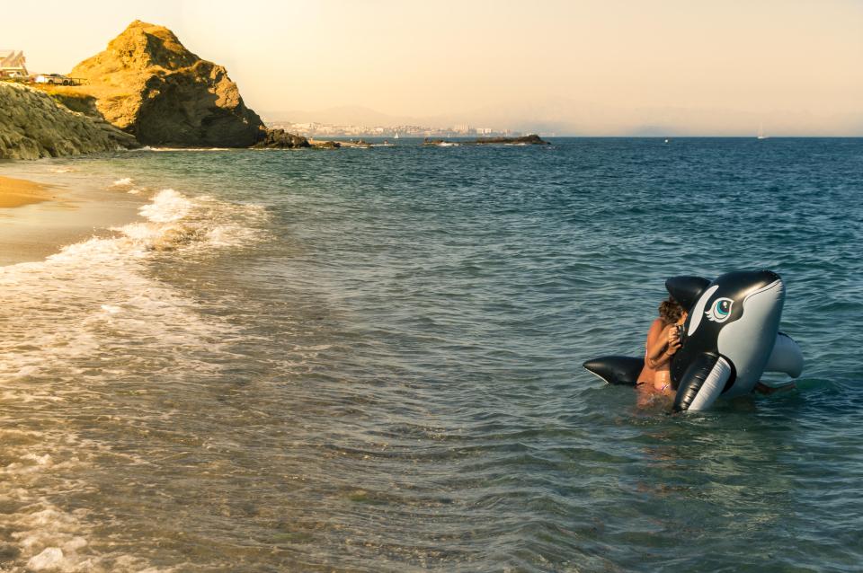 Children playing on a killer whale inflatable in the ocean.