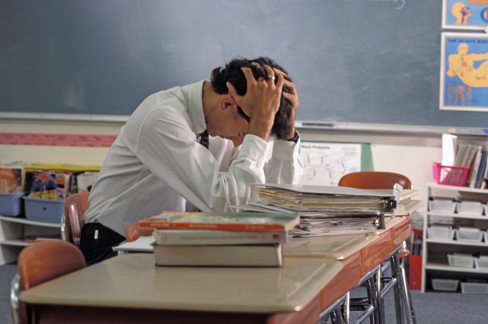 Stressed male teacher sitting at a desk in an empty classroom.