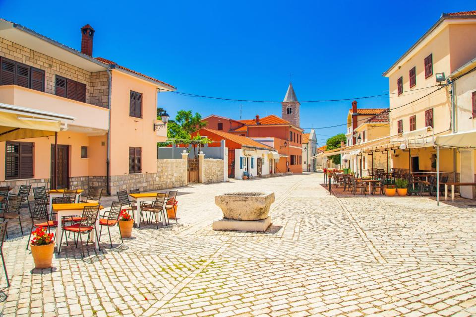 Cobbled square in Nin, Croatia, with cafes and a church tower.