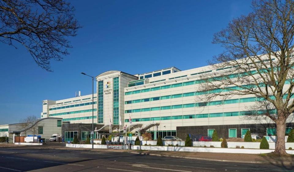 Hyatt Place hotel building seen from across a road, with trees in the foreground.