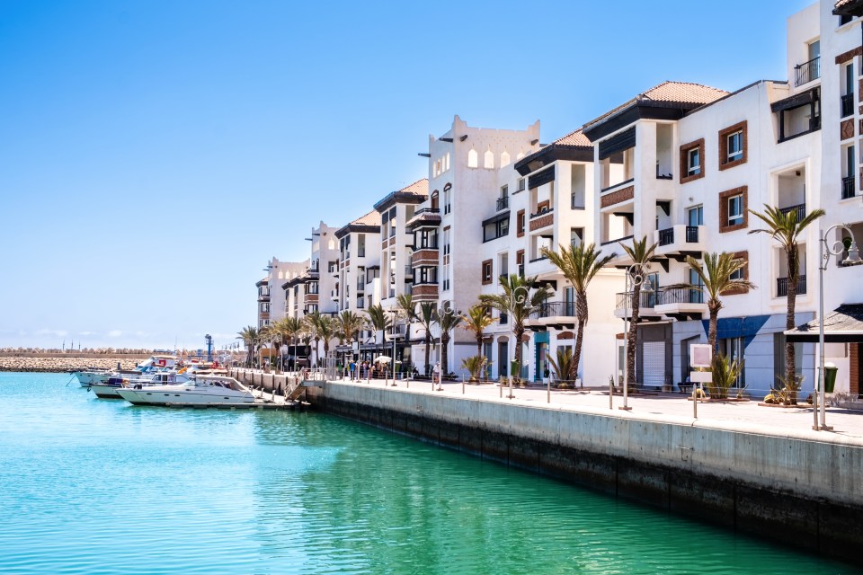 Agadir Marina with luxury apartments, boats in harbor, shops, and restaurants.