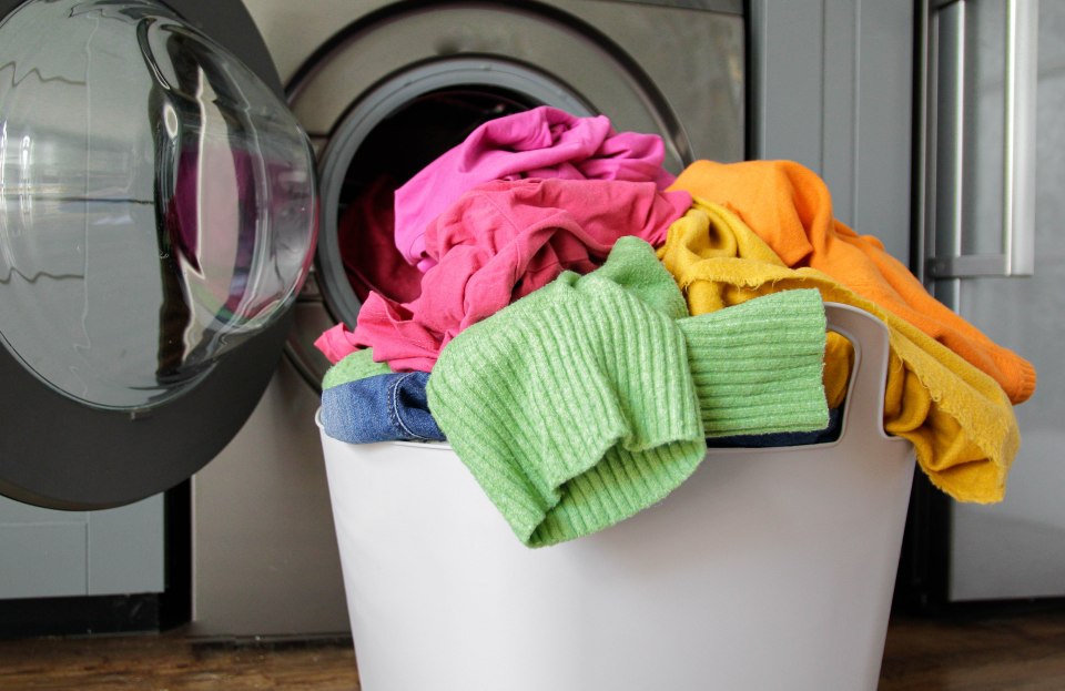 Laundry basket overflowing with colorful clothes next to a washing machine.
