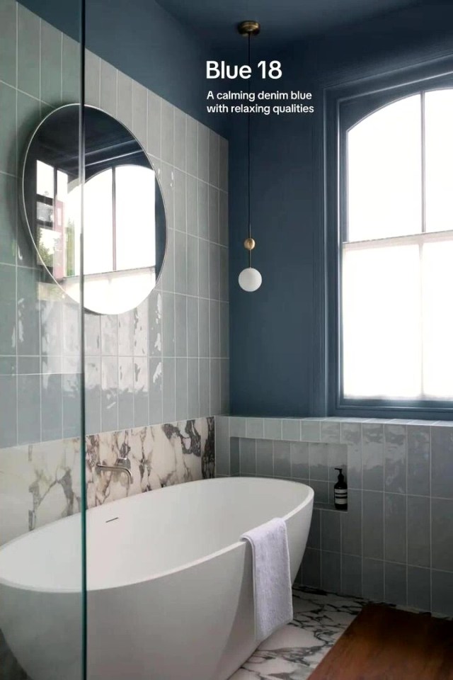 A modern bathroom featuring an oval bathtub, round mirror, and a window, with walls painted in LICK's "Blue 18".