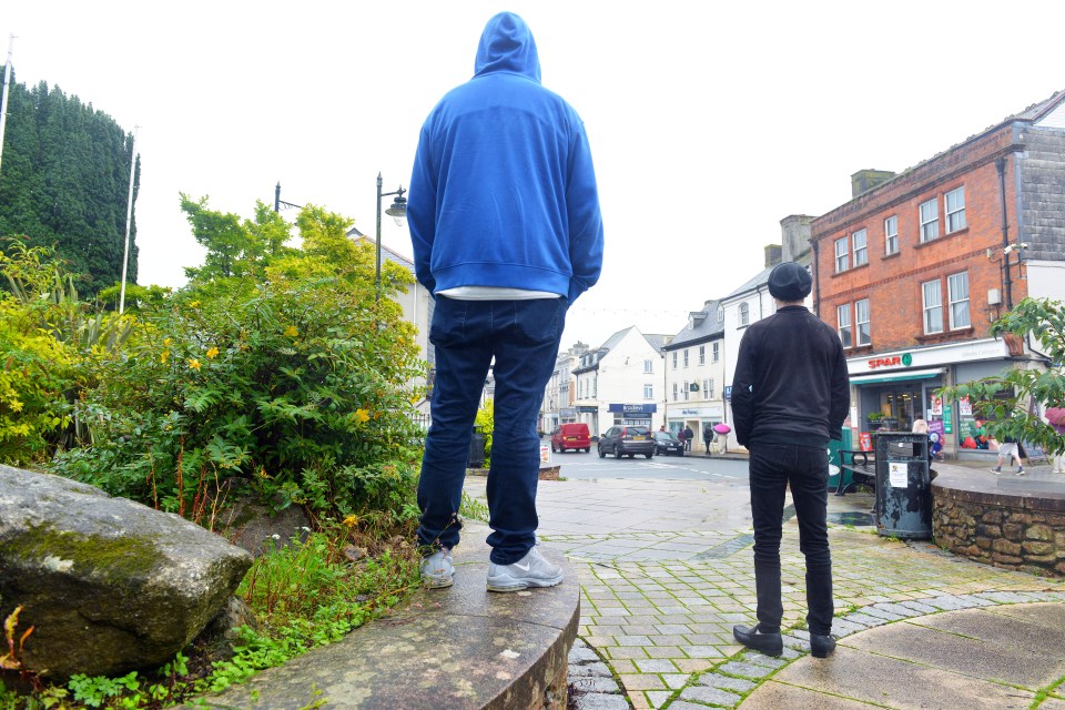 Two men stand with their backs to the camera, looking at a town street.