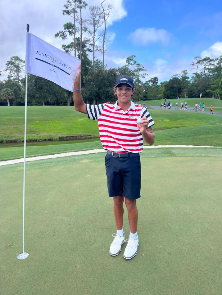 Golfer holding a golf ball and Junior Players Championship flag.