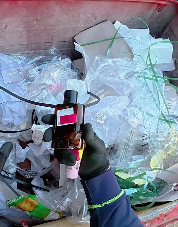 A gloved hand holds a bottle of aftershave found in a dumpster.