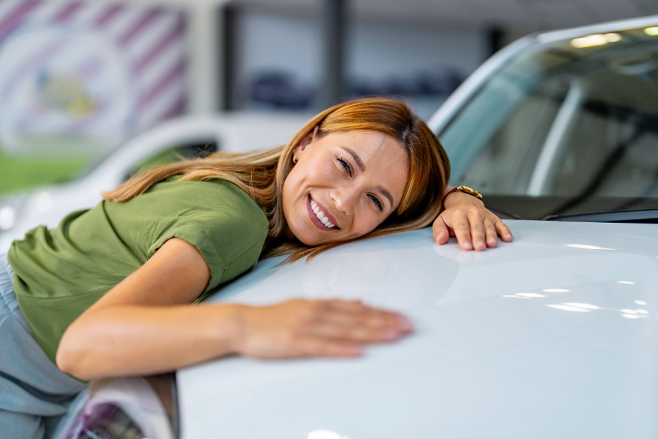 Happy young woman hugging her new white car.