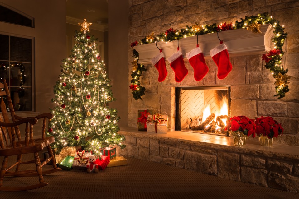 A glowing Christmas tree and fireplace with stockings and presents in a living room.